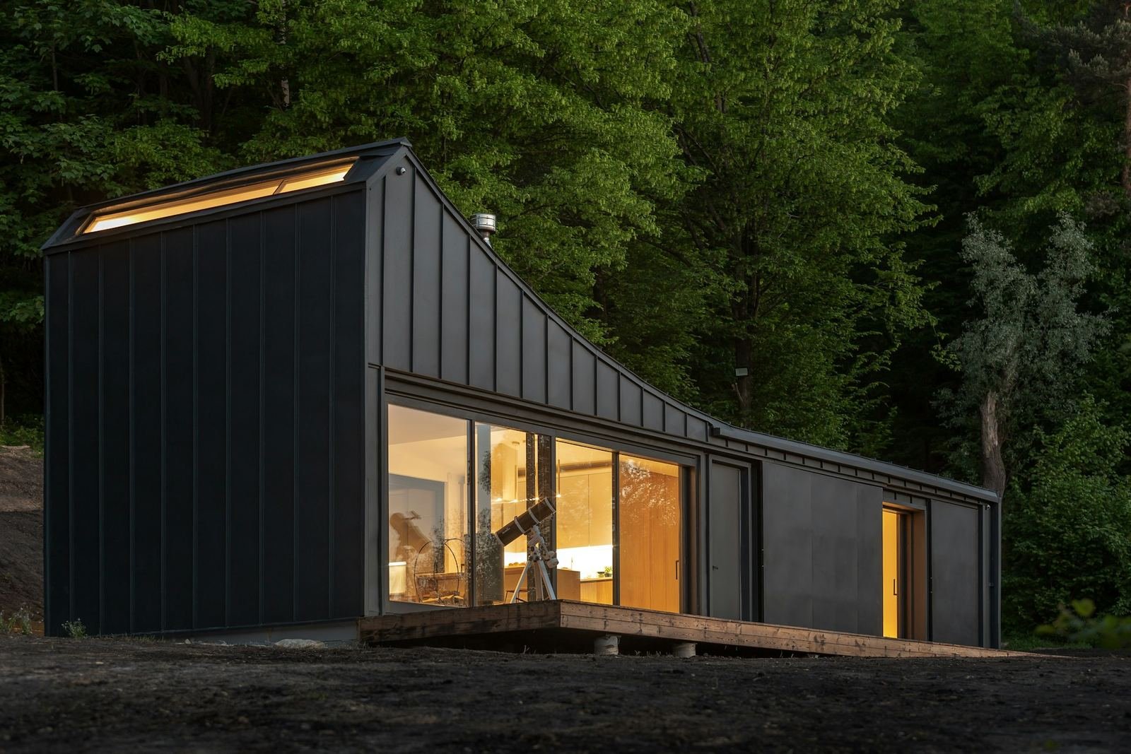 Black modular cabin with warm-lit windows in the woods
